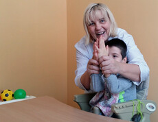 Eine Therapeutin arbeitet mit einem Kind im Kinderdorf Gomel an einer Therapie, indem sie mit ihm Hände schüttelt und spielerische Übungen macht.