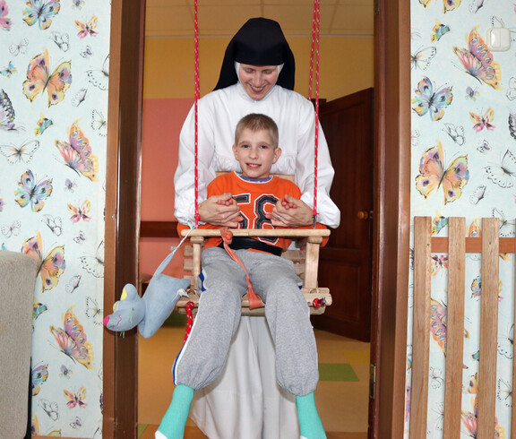 Eine Ordensschwester schwingt ein Kind sanft auf einer Schaukel und kümmert sich liebevoll um es im Kinderdorf Gomel.