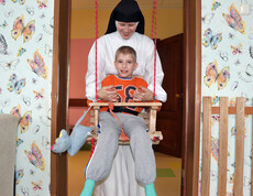 Eine Ordensschwester schwingt ein Kind sanft auf einer Schaukel und kümmert sich liebevoll um es im Kinderdorf Gomel.