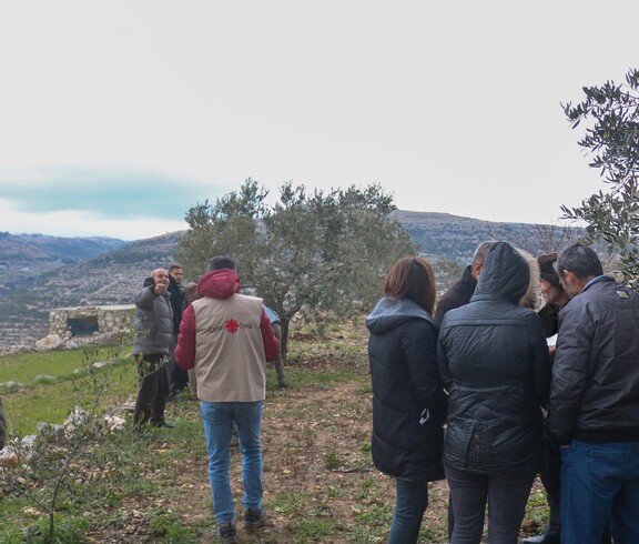 Gruppe diskutiert im Olivenhain unter Anleitung des Caritas-Teams Methoden der Umweltbewertung