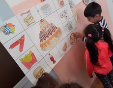 Zwei Kindergartenkinder stehen vor einem selbstgemalten Plakat, dass ungesunde Lebensmittel zeigt.