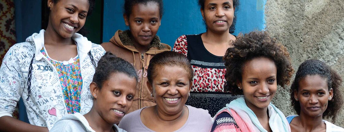 Mehrere Frauen und junge Menschen stehen gemeinsam lächelnd vor einer Hauswand