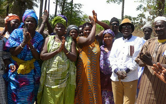 Gruppe von Menschen in der Region Ziguinchor, Senegal, die an einem Caritas-Projekt zur Errichtung von Brunnen und Dämmen teilnehmen und lächeln.