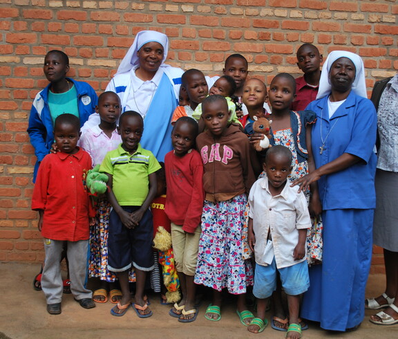 Eine Gruppe von Kindern und Erwachsenen steht gemeinsam vor einer Backsteinwand und blickt in die Kamera.