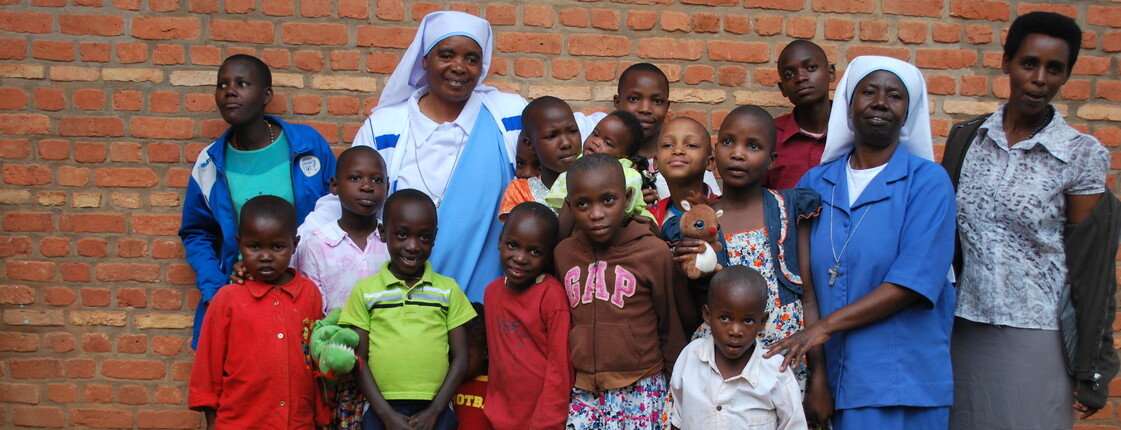 Eine Gruppe von Kindern und Erwachsenen steht gemeinsam vor einer Backsteinwand und blickt in die Kamera.