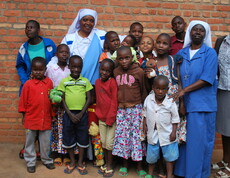 Eine Gruppe von Kindern und Erwachsenen steht gemeinsam vor einer Backsteinwand und blickt in die Kamera.