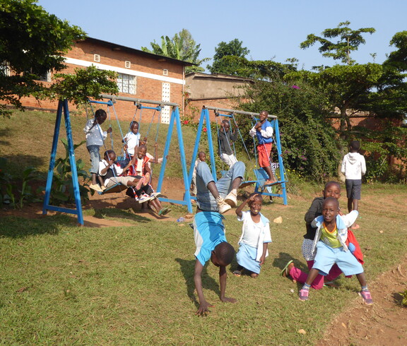 Mehrere Kinder spielen auf Schaukeln und im Freien auf einer Wiese.