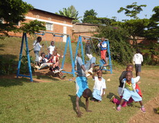 Mehrere Kinder spielen auf Schaukeln und im Freien auf einer Wiese.