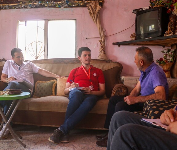 Caritas-Mitarbeitende im Gespräch mit Landwirt in traditionellem Wohnzimmer in Aramo