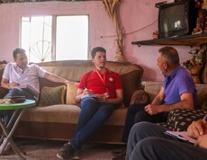Caritas-Mitarbeitende im Gespräch mit Landwirt in traditionellem Wohnzimmer in Aramo