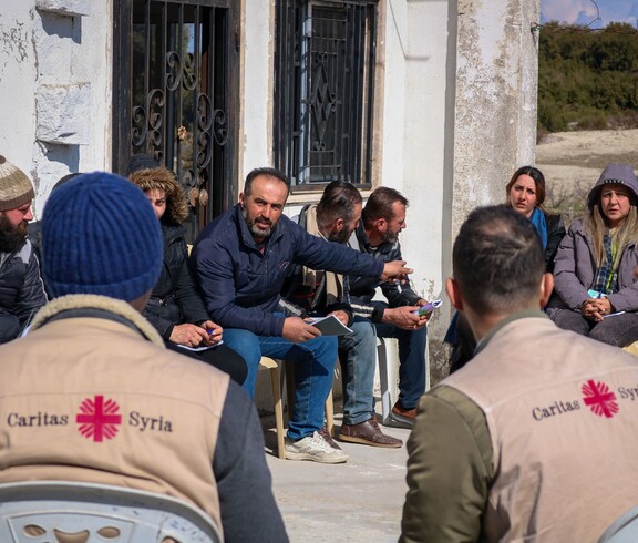 Diskussionsrunde zwischen Landwirt*innen und Caritas-Mitarbeitern vor einem Haus in Deir Touma