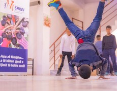 Ein Junge macht eine akrobatische Bewegung auf den Händen, während andere Kinder im Haus Eden Straßenkinderzentrum in Tirana zusehen.