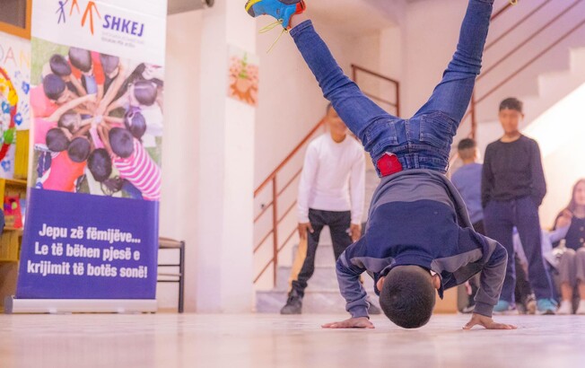 Ein Junge macht eine akrobatische Bewegung auf den Händen, während andere Kinder im Haus Eden Straßenkinderzentrum in Tirana zusehen.