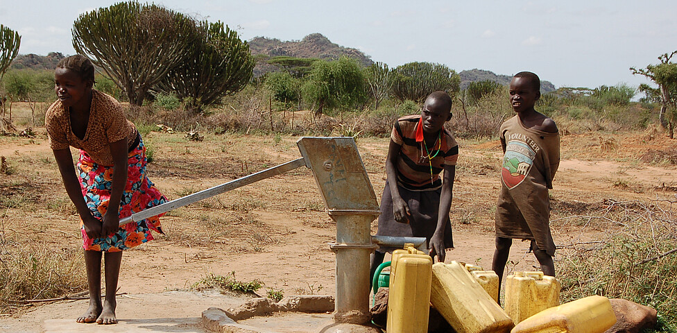 Kinder pumpen Wasser bei einem Brunnen mit einem schweren Hebel in Wasserkanister.