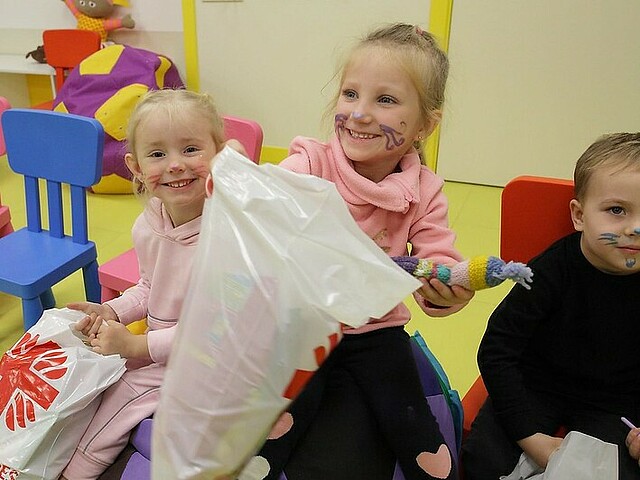 Das Foto zeigt drei Mädchen in einem Raum mit Spielzeug und Kindersessel, sie lachen in die Kamera.