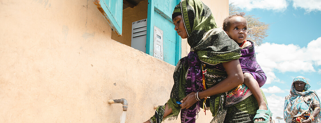 Eine Frau in afrikanischem Gewand füllt einen Kanister mit Wasser